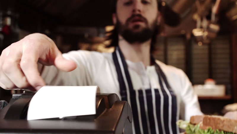 A chef tearing an order ticket from a kitchen printer